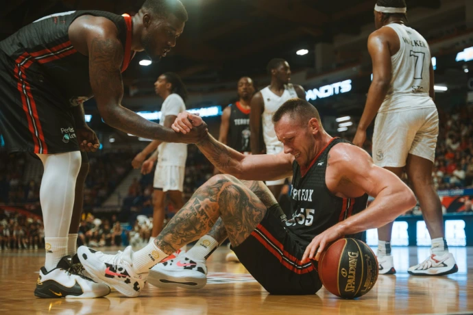 A basketball player helps his teammate up from the floor.